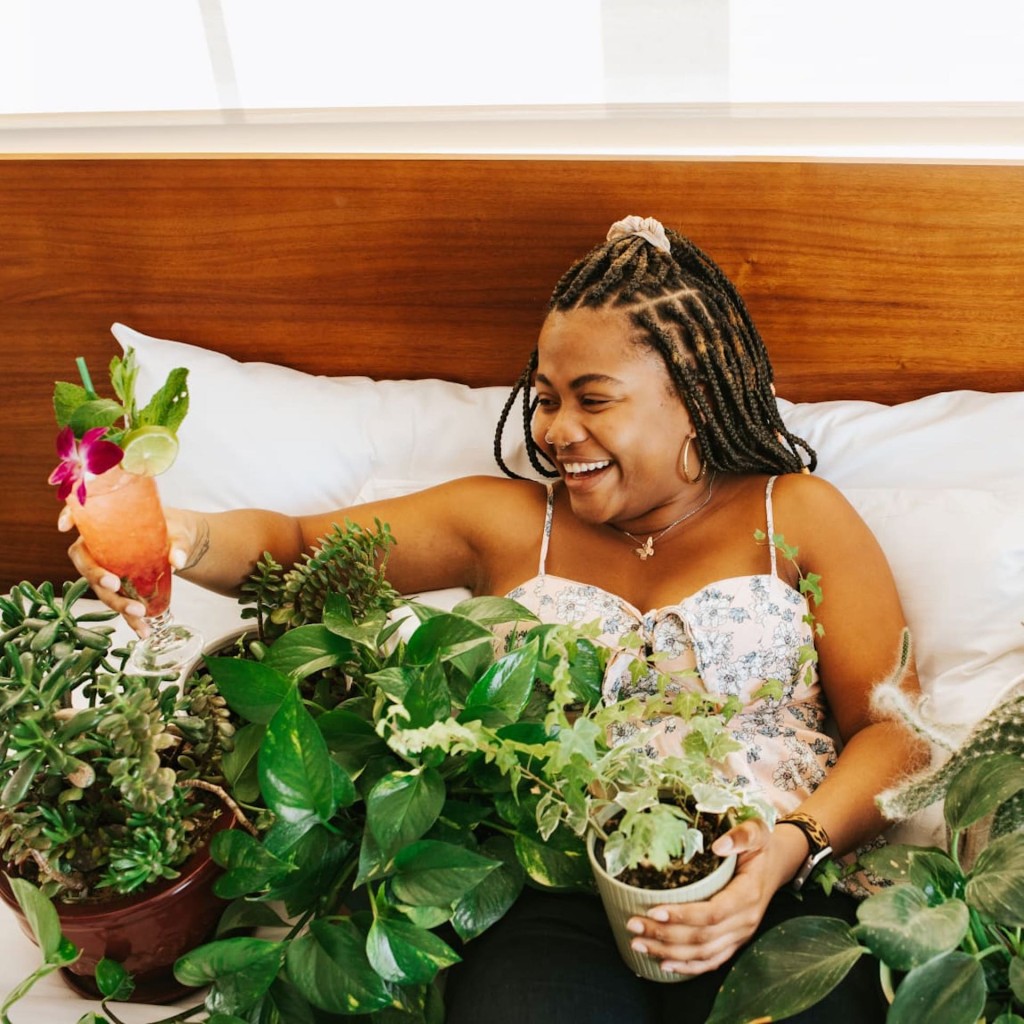 Woman in hotel bed surrounded by houseplants.