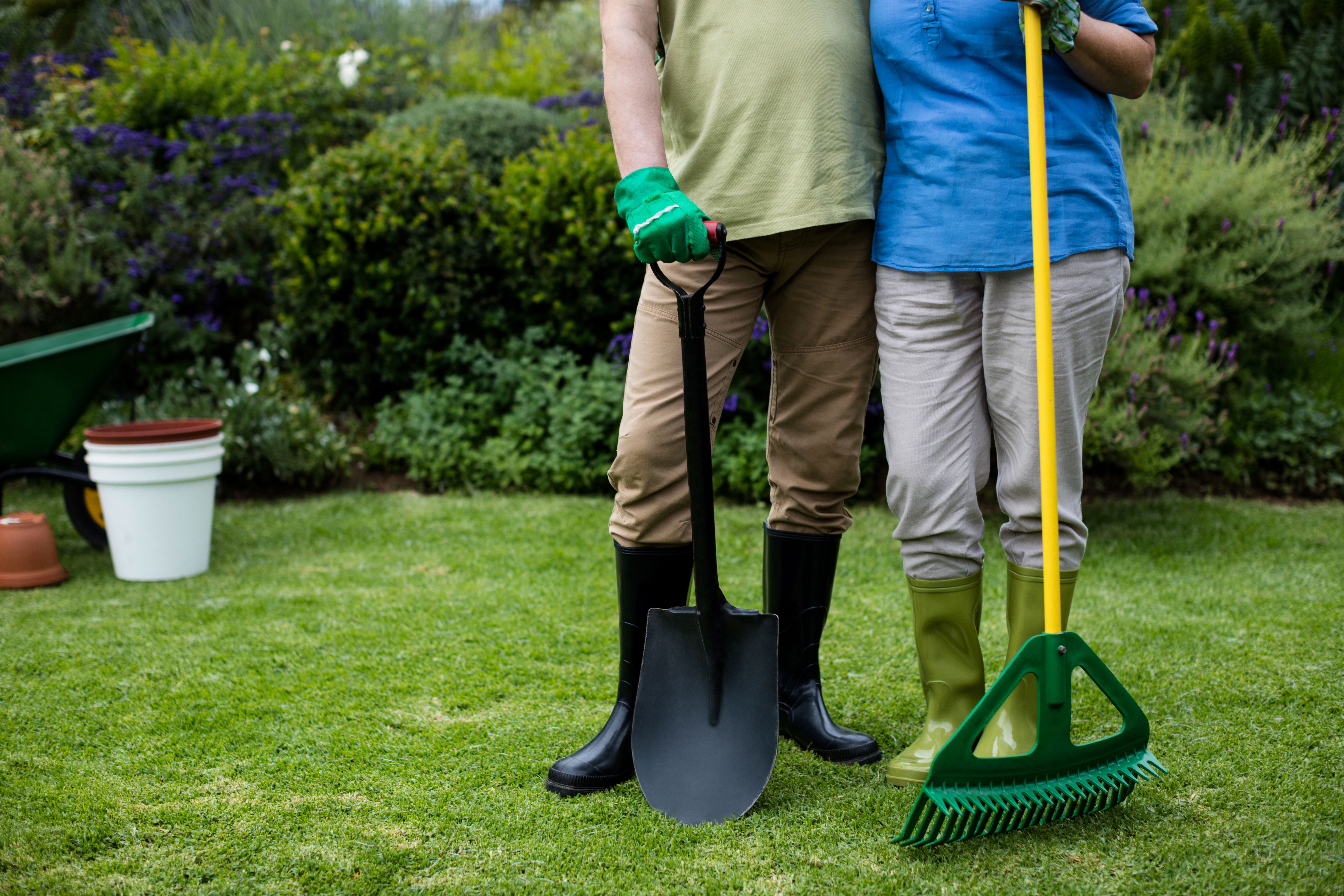 Couple standing on a lawn with garden tools.