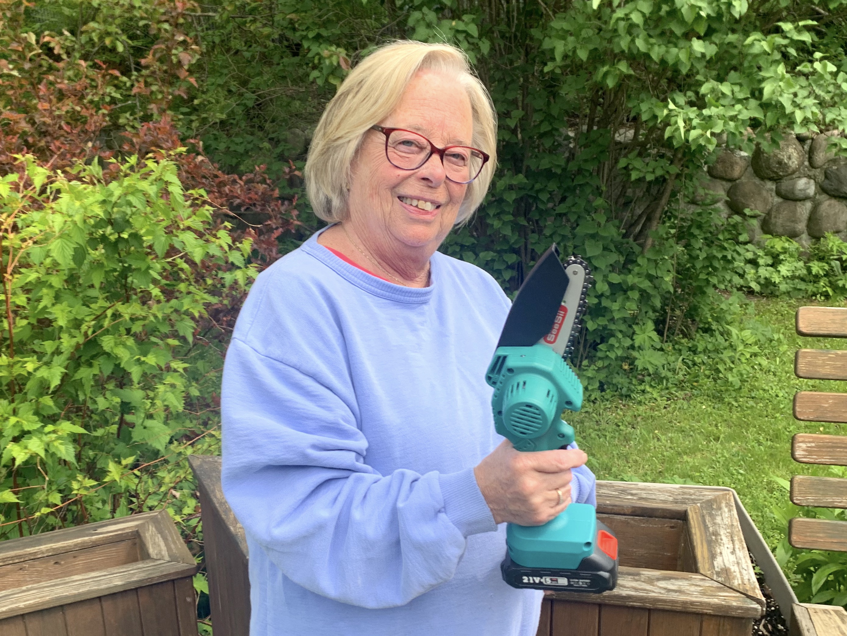 Senior woman hold cordless mini chainsaw.